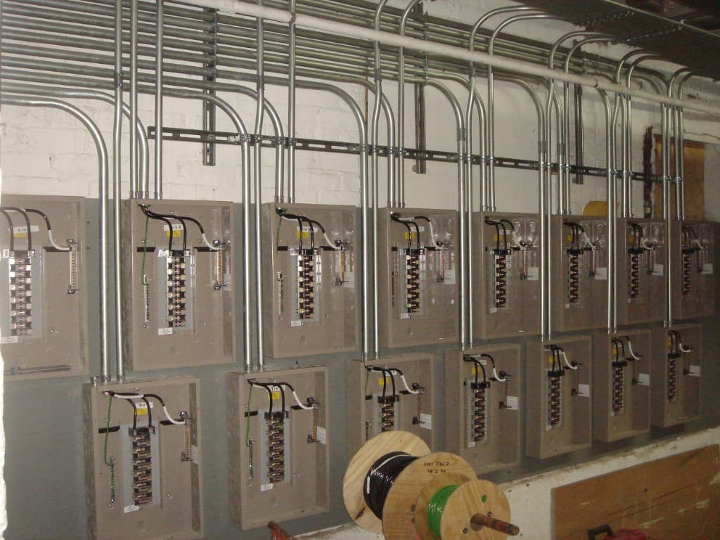 Rows of commercial electrical breaker panels with organized conduit runs on a facility wall
