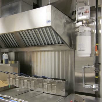 Commercial kitchen exhaust hood with Range Guard fire suppression cylinder mounted on the wall